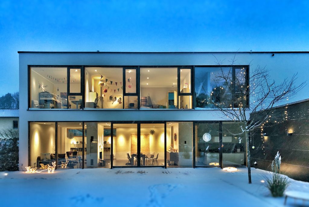 Frontalansicht eines Einfamilienhauses im Schnee mit brennender Innenbeleuchtung